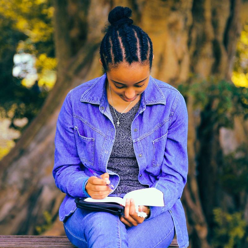 A young woman writing in a notebook with her Bible open